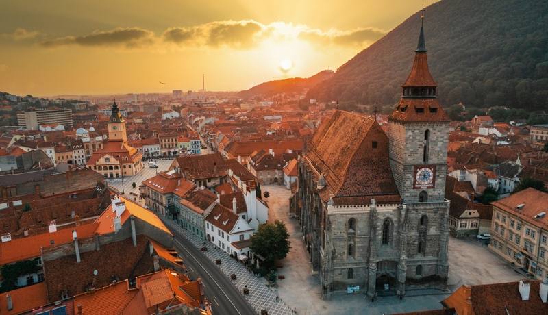 aerial-drone-view-black-church-old-brasov-centre-sunset-romania-old-residential-buildings-around-it-hills-with-greenery