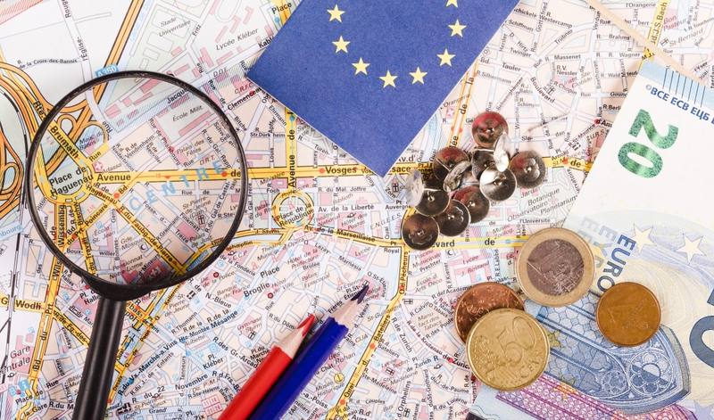 euro-currencies-with-magnifying-glass-pushpins-pencils-flag-world-map