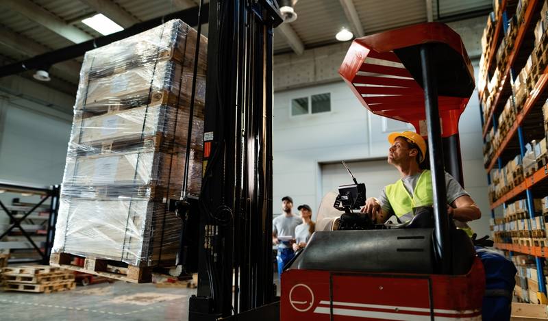 forklift-operator-loading-cargo-while-working-warehouse-his-colleagues-are-background