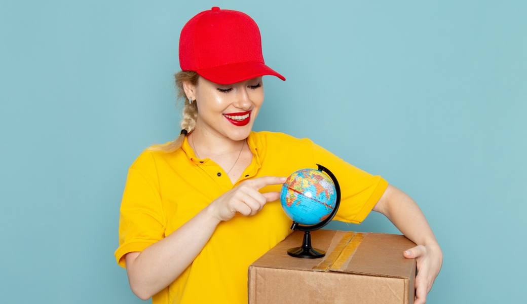front-view-young-female-courier-yellow-shirt-red-cape-holding-little-globe-package-smiling-blue-space