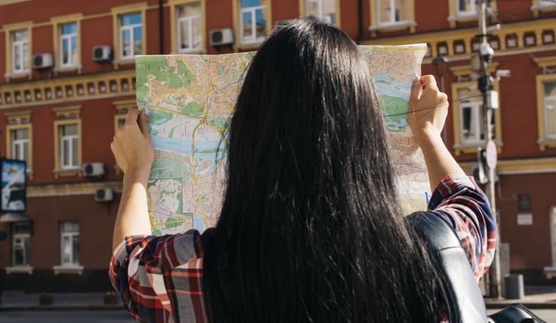 rear-view-woman-reading-map-with-background-red-building-exterior