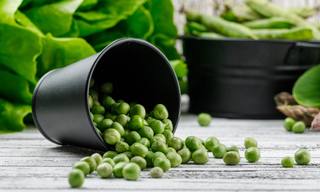 scattered-peas-from-bucket-with-asparagus-bok-choy-lettuce-green-pods-side-view-wooden-wall