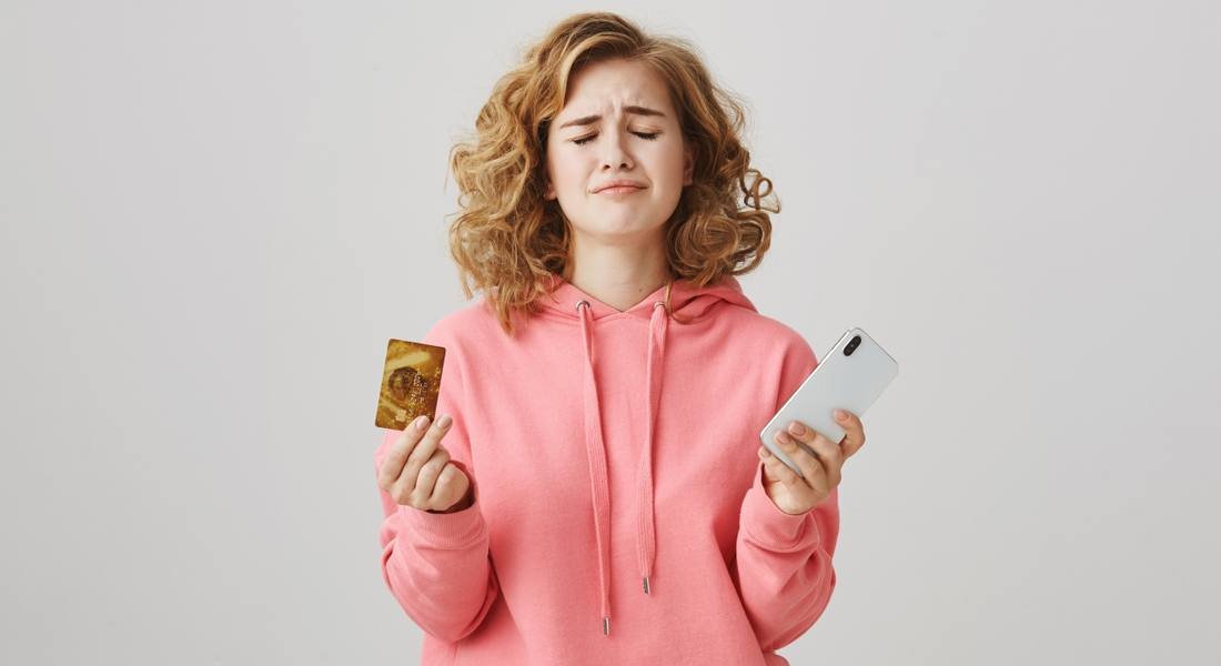 upset-curly-haired-girl-frowning-lacking-money-bank-account-hold-mobile-phone