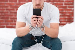wp-448544ab9c6c521e-man-holding-his-phone-while-he-is-tied-up-with-chains