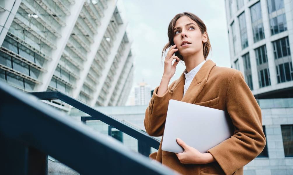 wp-774ed32380b5e435-young-pensive-casual-businesswoman-coat-with-laptop-talking-cellphone-thoughtful