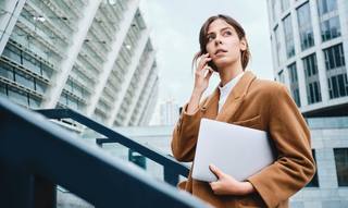 wp-774ed32380b5e435-young-pensive-casual-businesswoman-coat-with-laptop-talking-cellphone-thoughtful