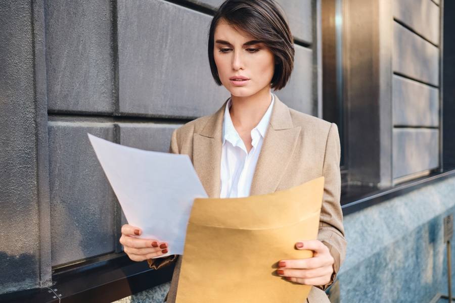 wp-da56187426c76c6b-young-serious-businesswoman-suit-thoughtfully-working-with-papers-city-street