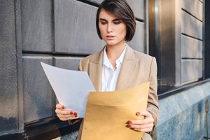 wp-da56187426c76c6b-young-serious-businesswoman-suit-thoughtfully-working-with-papers-city-street